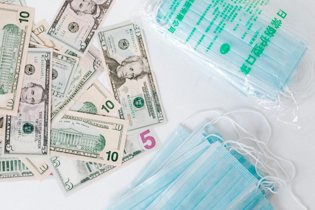 zipwp-image-4386398 From above composition of stack of USA dollar bills placed near medical protective masks produced in China illustrating concept of medical expenses and deficit during COVID 19